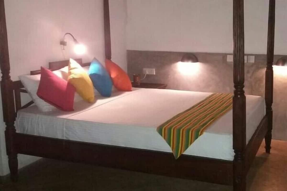 A four-poster bed with a white bedspread and colorful pillows. There are two bedside lamps on either side of the bed.