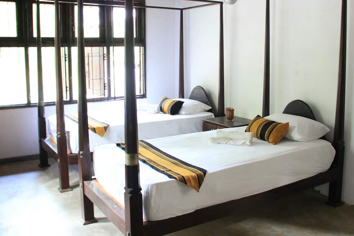 A four-poster bed with white linens and striped pillows, a bedside table with a lamp, and a window with bars.