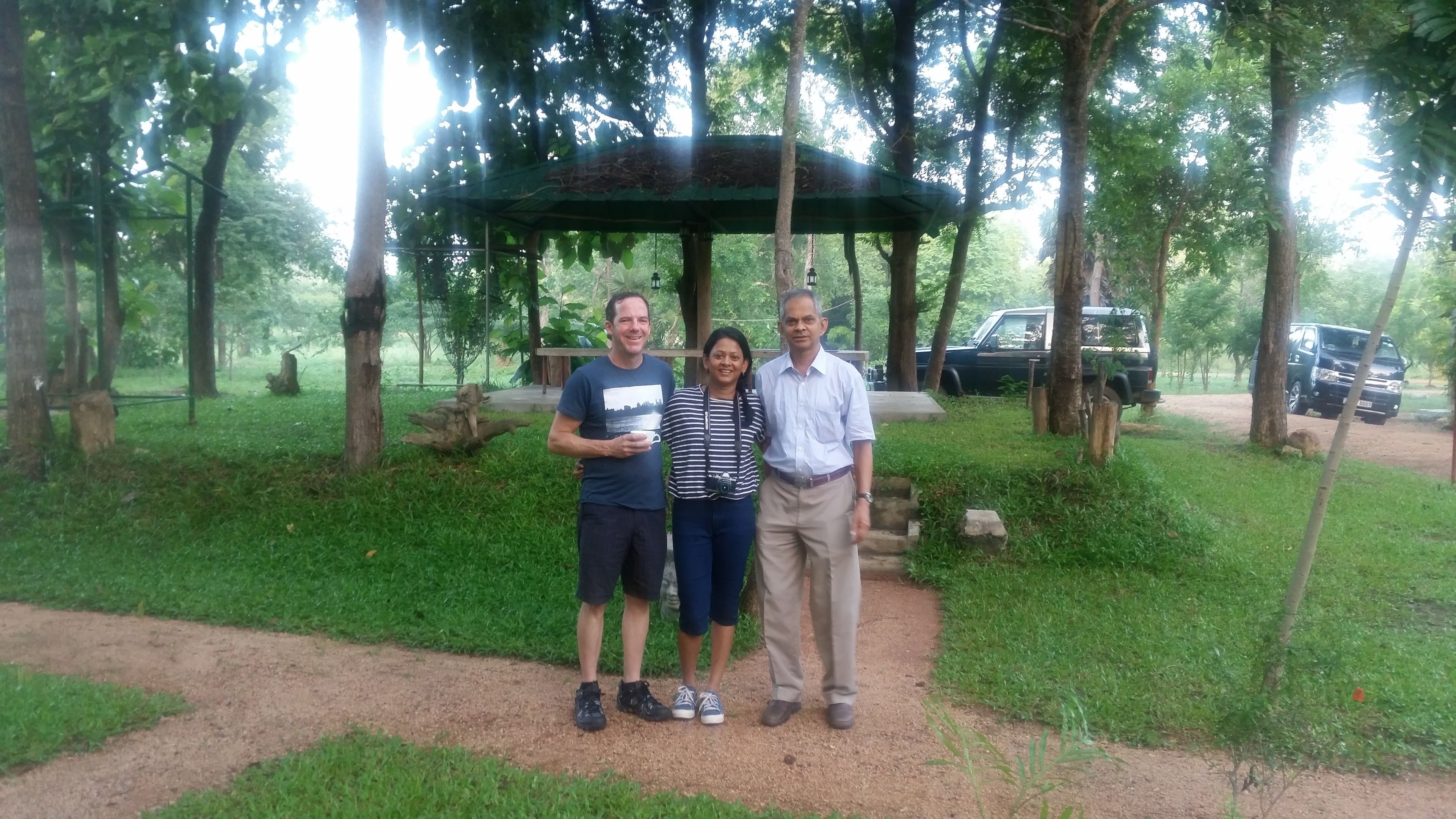 Un grupo de personas de pie en un parque con un quiosco y un sendero de tierra.