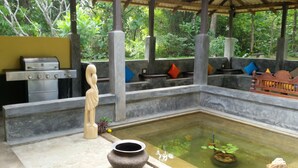 Un espace extérieur abrité comprenant un barbecue, une statue, un petit étang avec des poissons et un bassin en pierre.
