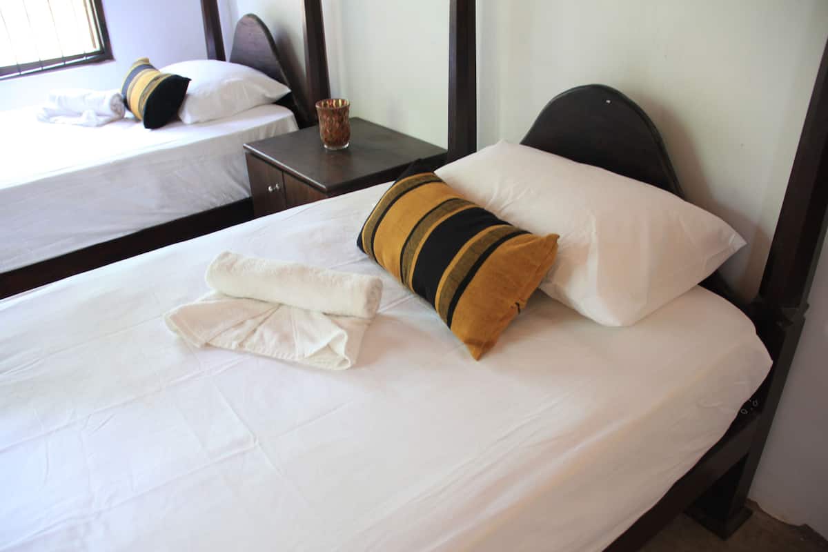 A hotel room with two single beds, each with white bedding and striped pillows. There is a neatly folded towel on the bed in the foreground.