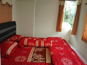 A bed with red bedding and a headboard, a window with curtains, and a white wall. - Villa Tamie Bumi Ciherang (Cipanas)