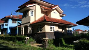 A two-story house with a red-tiled roof, a stone foundation, and a small garden area with a pathway. - Villa Tamie Bumi Ciherang (Cipanas)