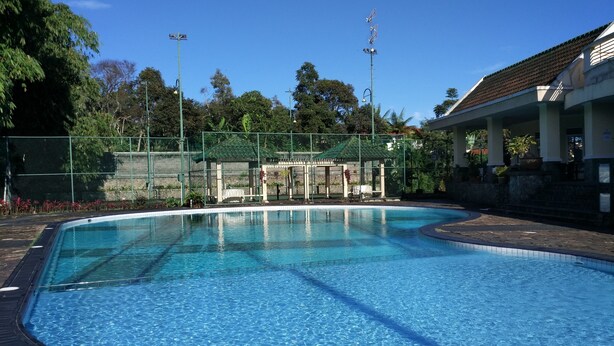 A swimming pool with a tiled deck, surrounded by a fence and trees. - Villa Tamie Bumi Ciherang (Cipanas)
