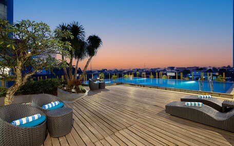 A rooftop pool area with lounge chairs and a view of the cityscape at dusk.