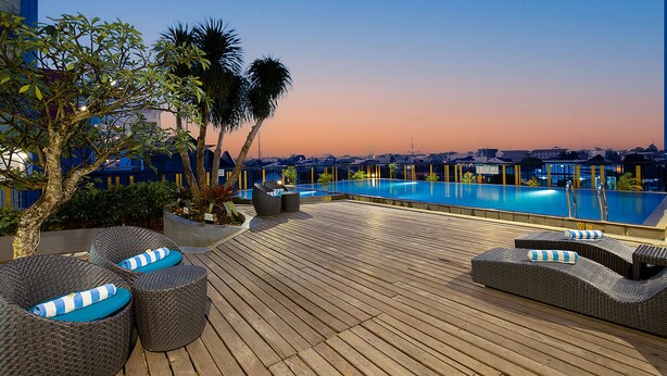 A rooftop pool area with lounge chairs and a view of the cityscape at dusk.