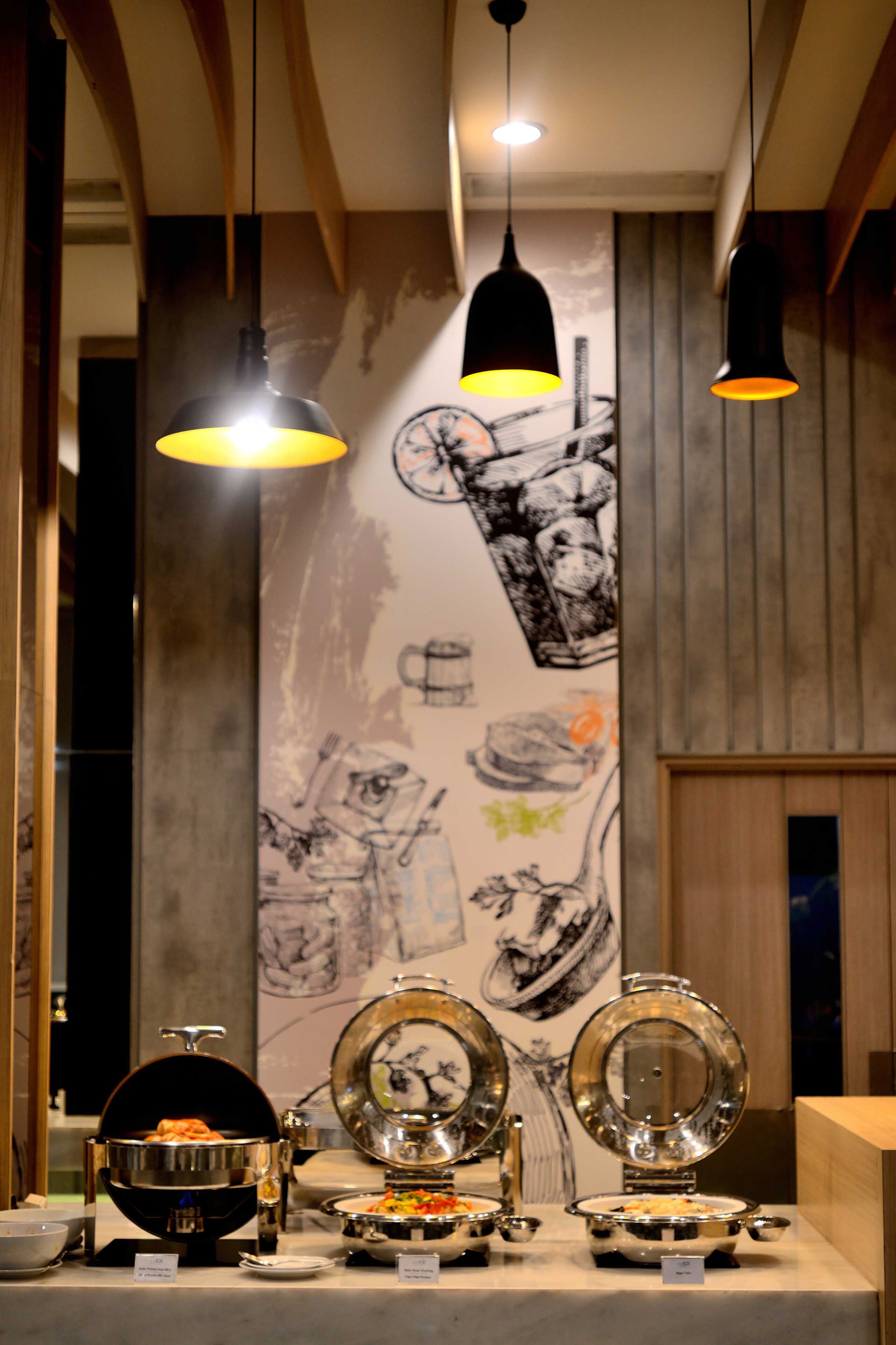 A buffet setup with multiple serving stations, a large wall mural, and pendant lighting.