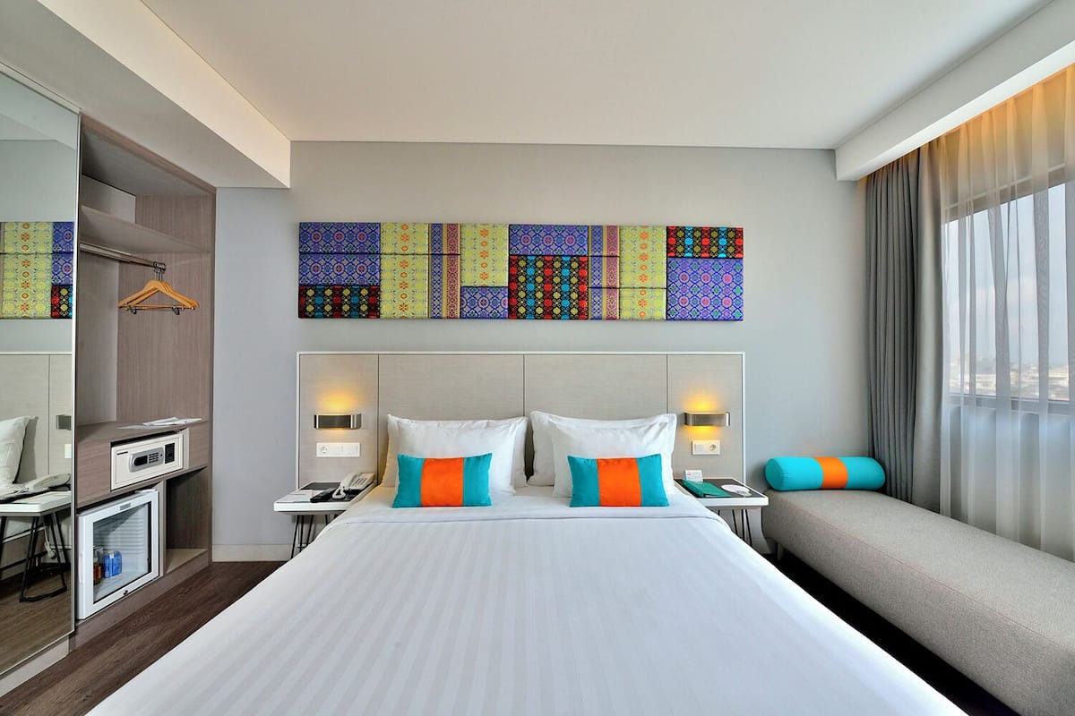 A hotel room with a large bed, bedside tables, a desk, a chair, a TV, and a window with curtains.