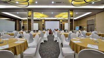 A conference room with multiple tables and chairs, equipped with nameplates, water glasses, and a projector screen.