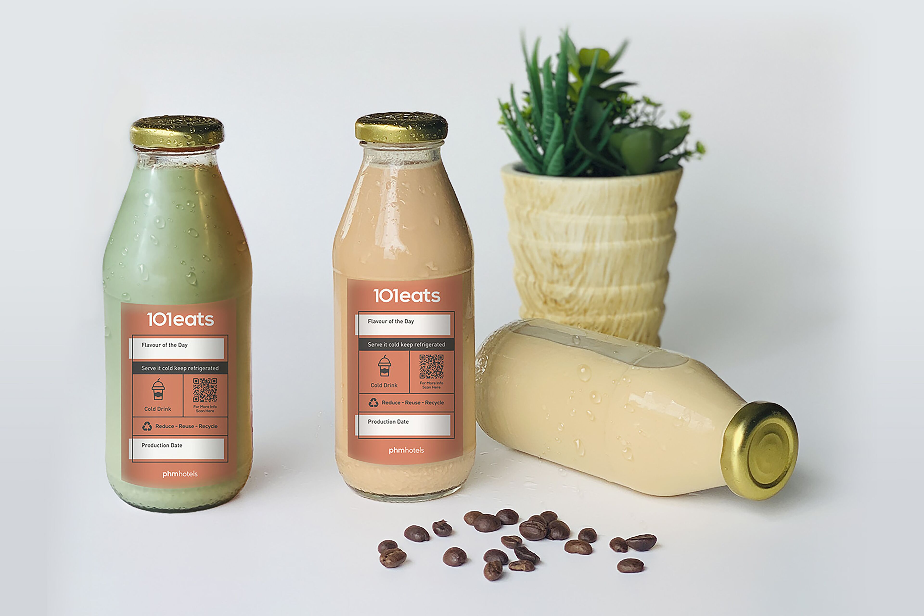 Dos botellas de bebidas 101eats y una planta en maceta sobre una superficie blanca.
