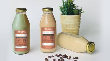 Two bottles of 101eats beverages and a potted plant on a white surface.