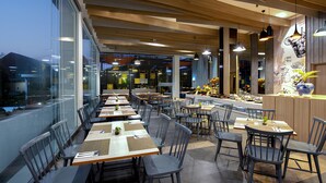 A modern restaurant with a long counter, multiple tables, and chairs.