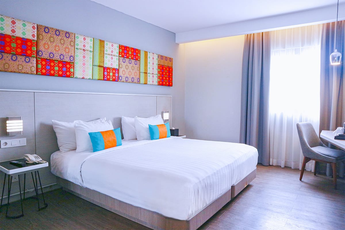 A hotel room with a large bed, a desk with a chair, a telephone, and a wall-mounted light fixture.