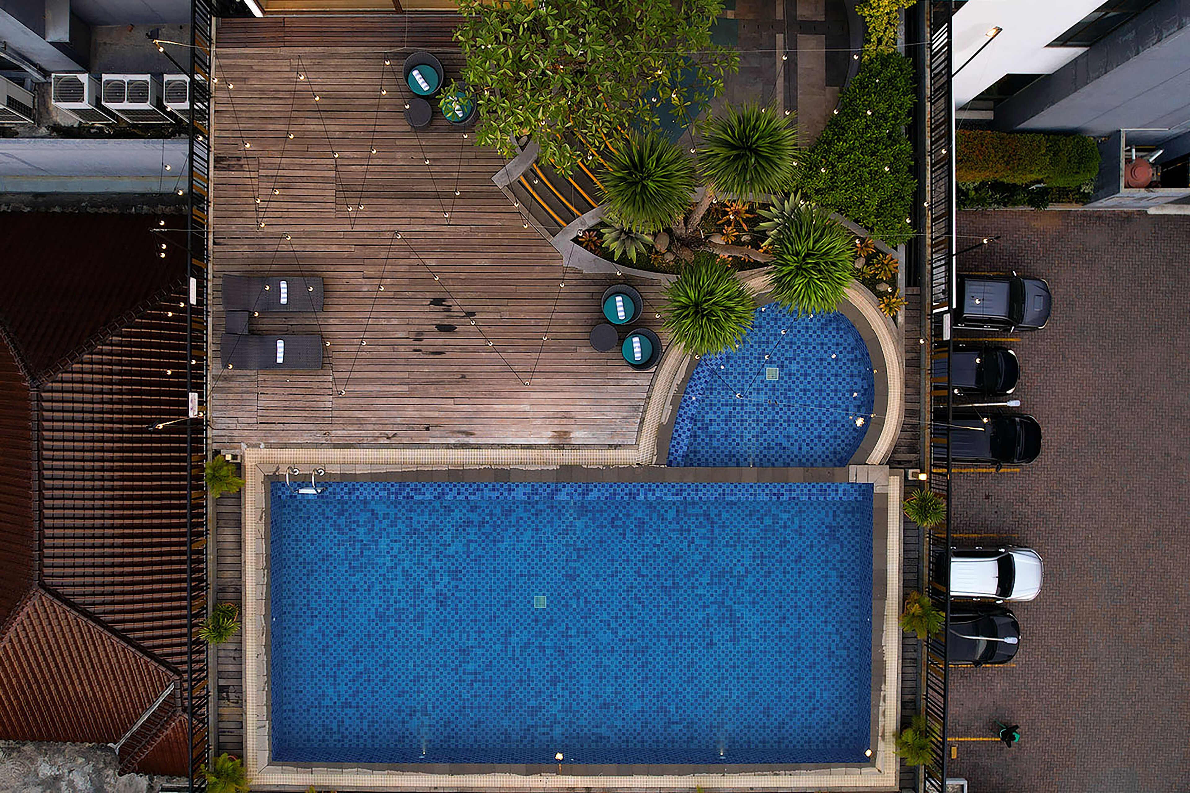 Ein Pool auf dem Dach mit einer Holzterrasse, Sitzbereichen und einigen geparkten Autos in der Nähe.
