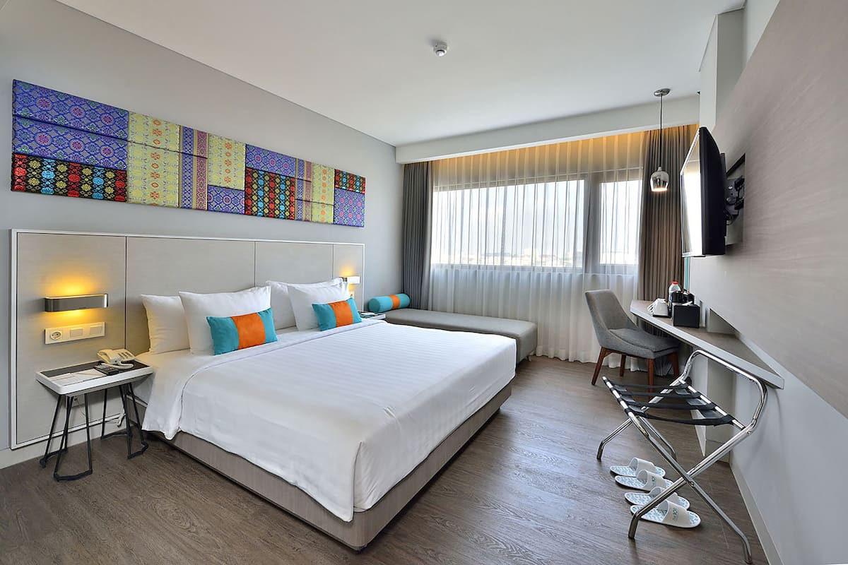 A modern hotel room with a large bed, bedside lamps, a desk with a chair, and a television.