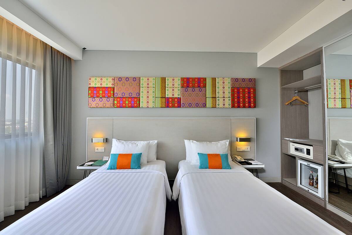 A hotel room with two beds, a minibar, and a large window with curtains.