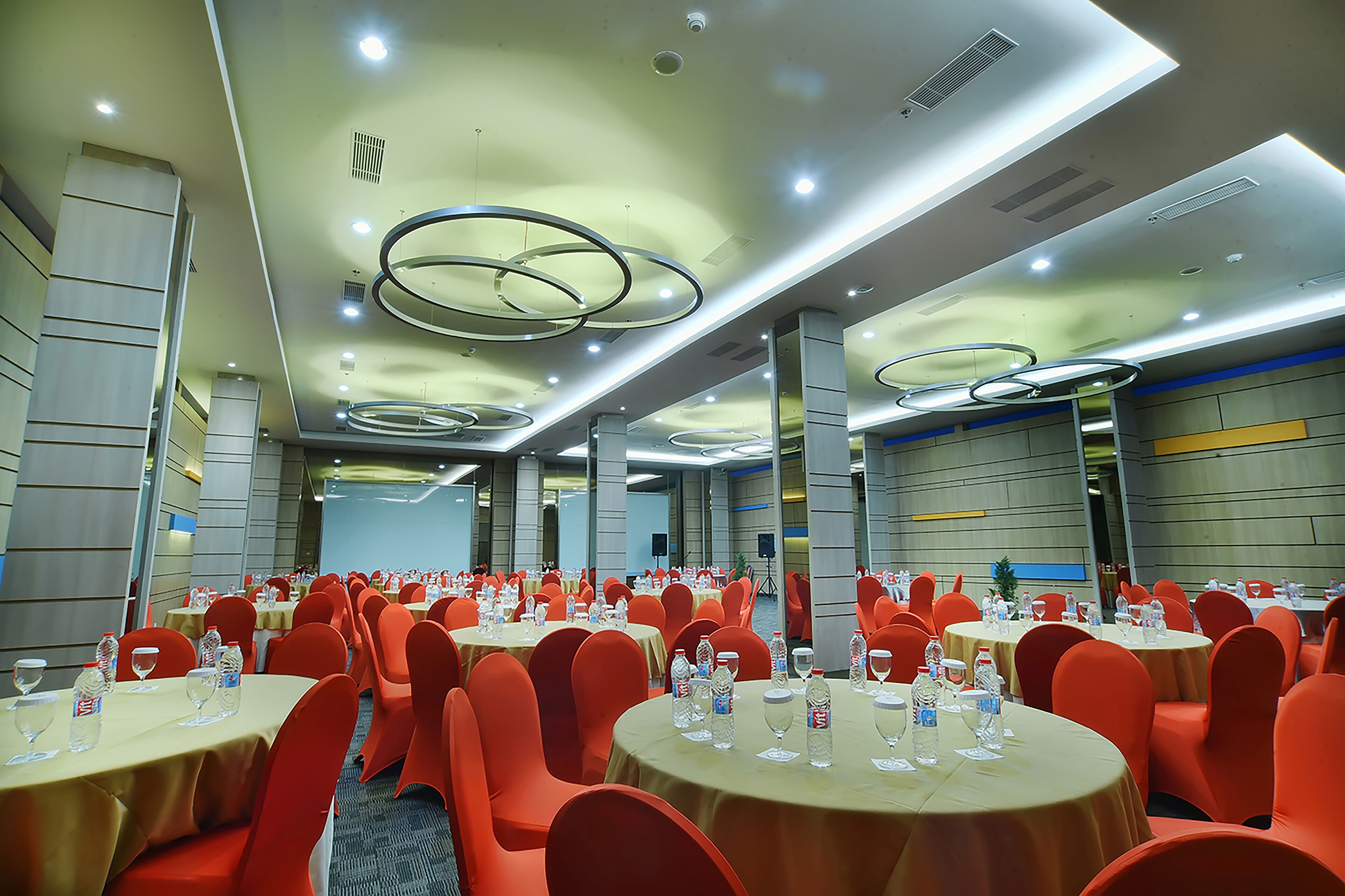 A conference room with round tables, red chairs, and water bottles on each table.