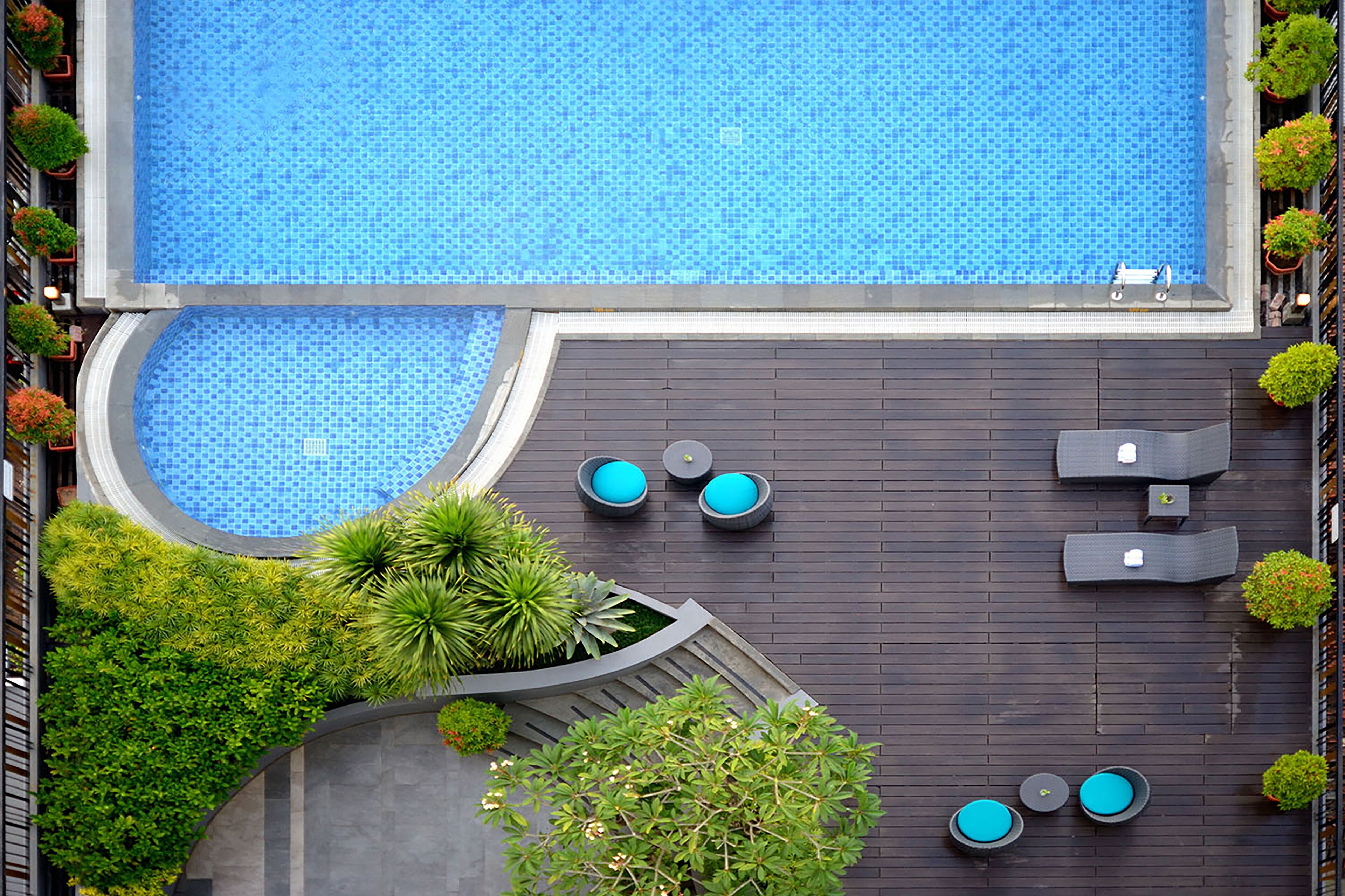 Ein Pool auf dem Dach mit blauem Mosaikfliesenmuster, umgeben von dunklem Holzboden und ausgestattet mit mehreren Liegestühlen und runden Tischen.