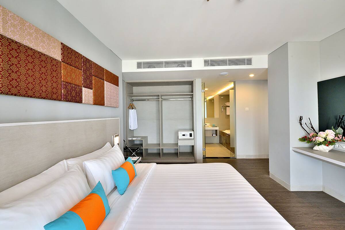 A modern hotel room with a large bed, a walk-in closet, a bathroom, and a TV on a stand.