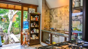 A kitchen with a gas stove, a water dispenser, and a shelf with various kitchen items. - Griya Sriwedari (Ubud)