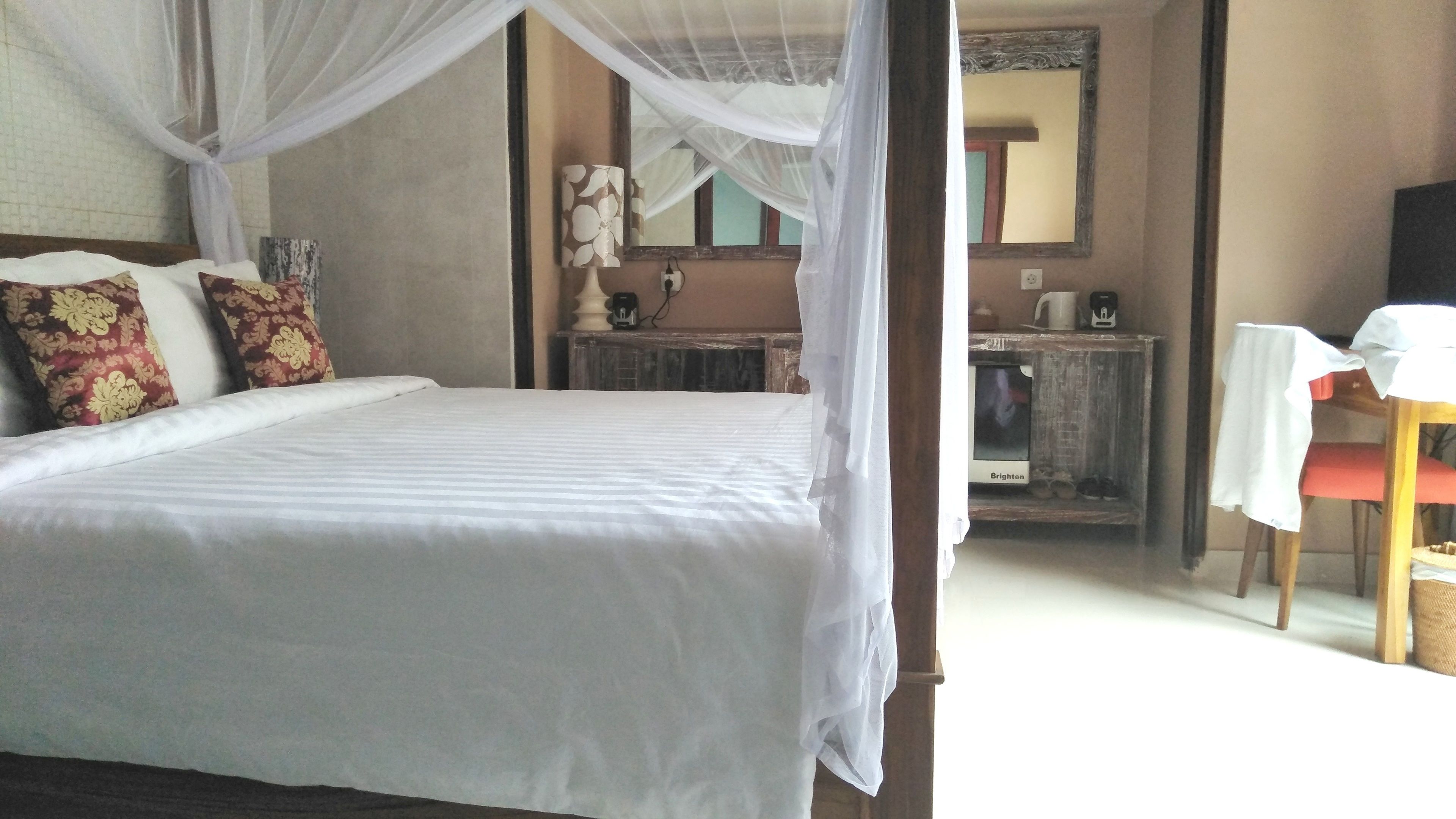 Un dormitorio con cama, mesita de noche, silla, espejo y ventana con vistas al exterior.