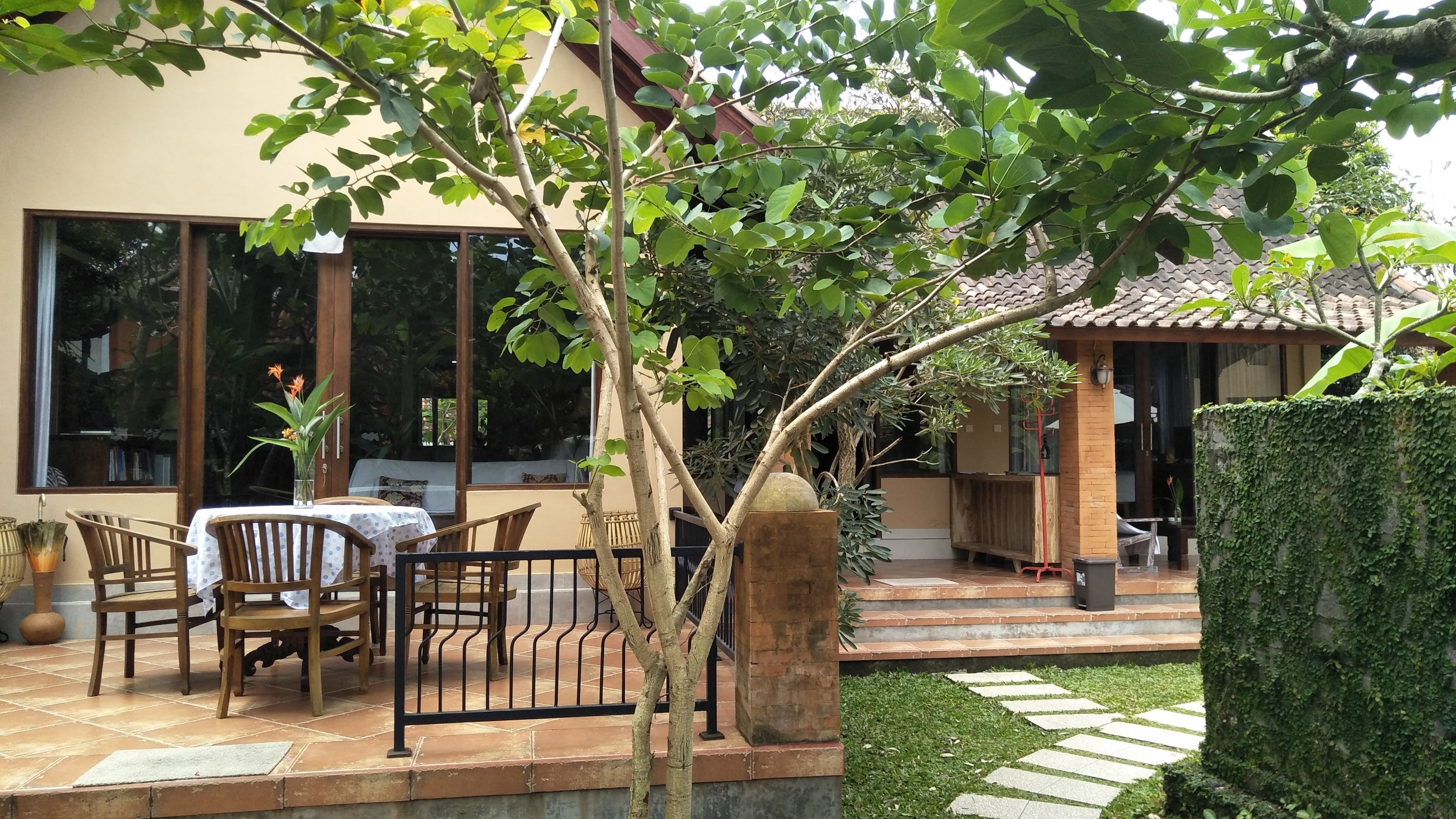 Eine Terrasse mit Tisch und Stühlen, ein Steinweg und ein grüner Heckenstreifen.