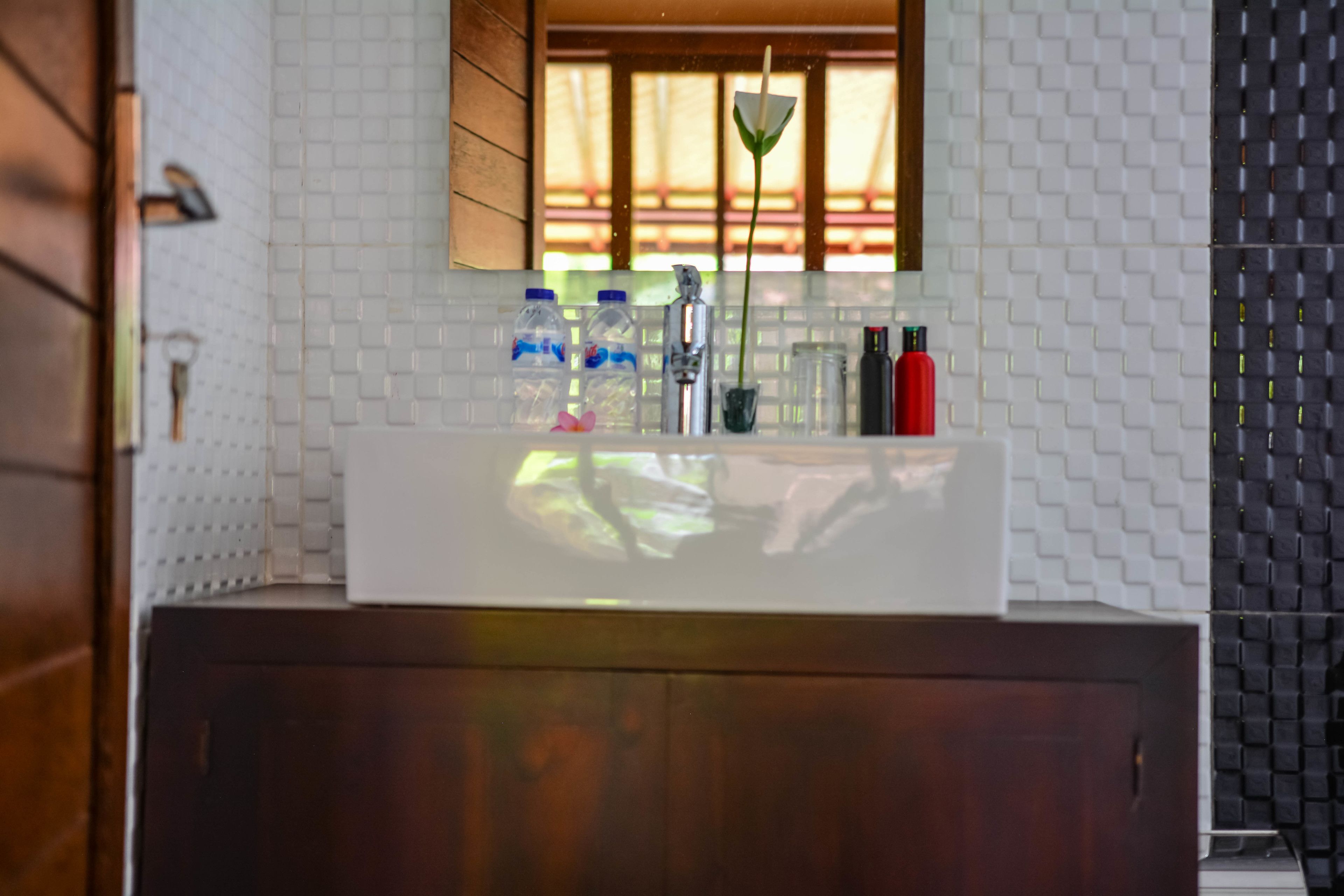Une salle de bain avec un mur recouvert de carreaux blancs, un meuble en bois, un lavabo blanc avec un robinet et un miroir au-dessus du lavabo.