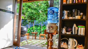 A kitchen with a water dispenser, a refrigerator, and a shelf with kitchen appliances. - Griya Sriwedari (Ubud)