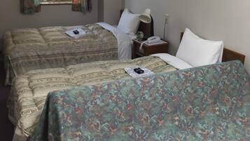 A hotel room with two beds, a bedside table with a lamp, and a window with curtains.