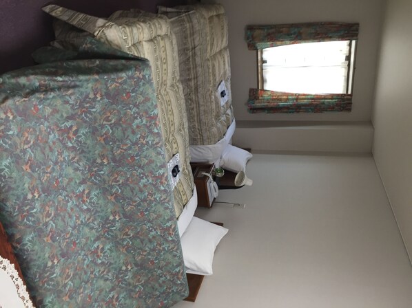 A small, cozy room with two beds, a window with a view, and a small table with a lamp.