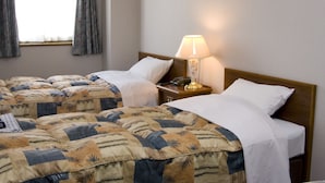 Habitación de hotel con dos camas, una mesita de noche con lámpara y una ventana con cortinas.