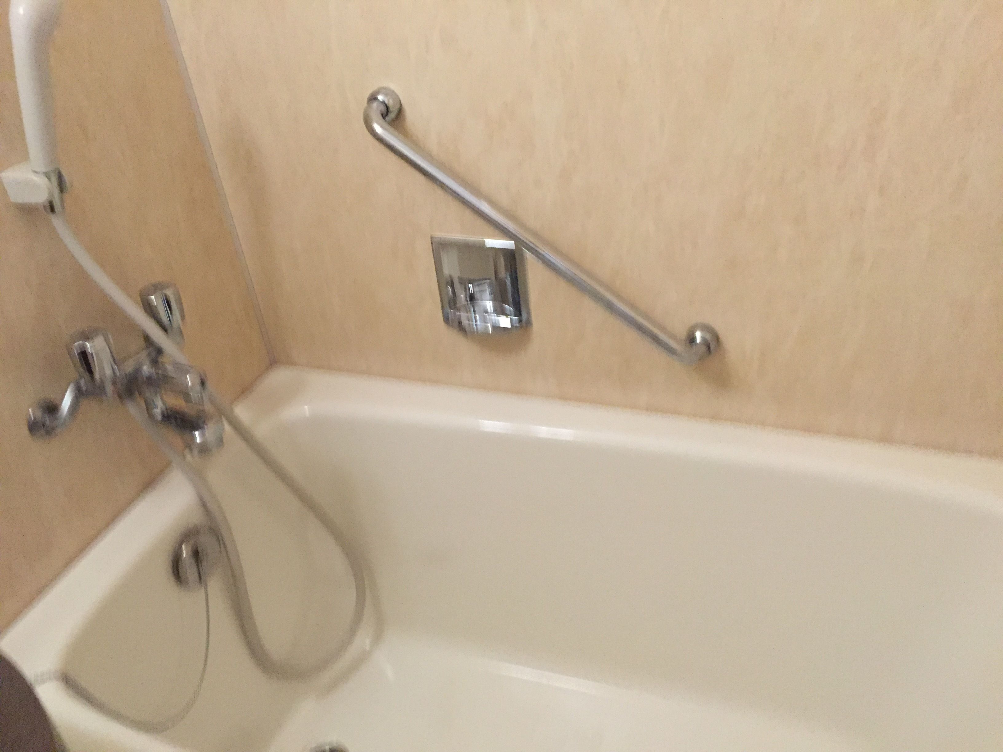 A bathtub with a handheld showerhead, a grab bar, and a wall-mounted faucet.