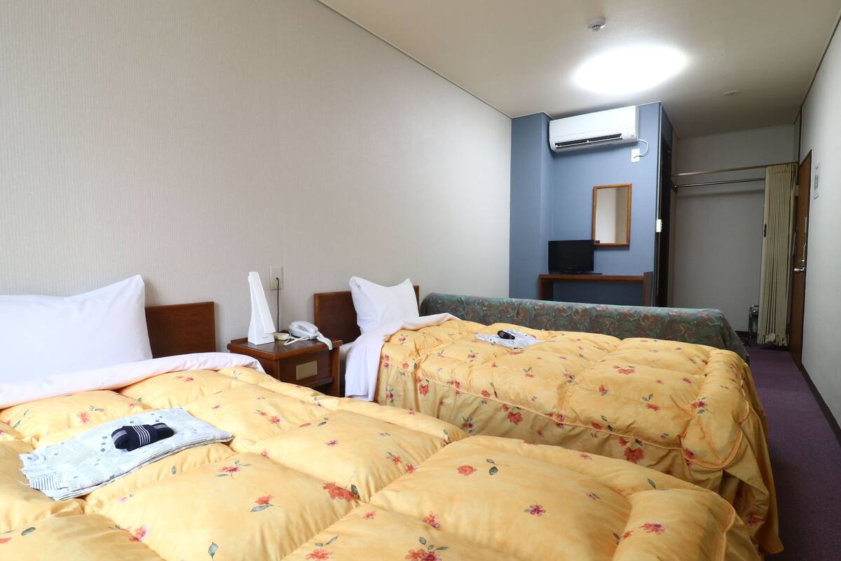 Quarto de hotel com duas camas, uma mesa de cabeceira com abajur, telefone e televisão.