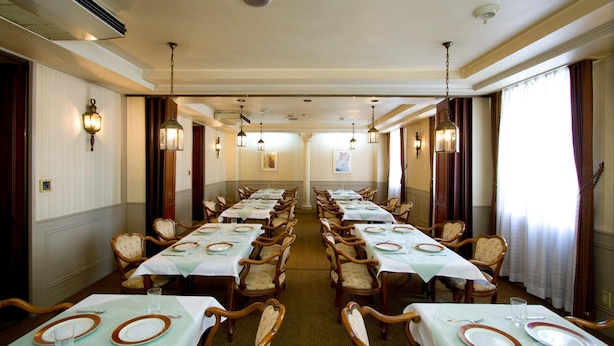 Un comedor amplio con mesas dispuestas para una comida, sillas de madera y lámparas colgantes.