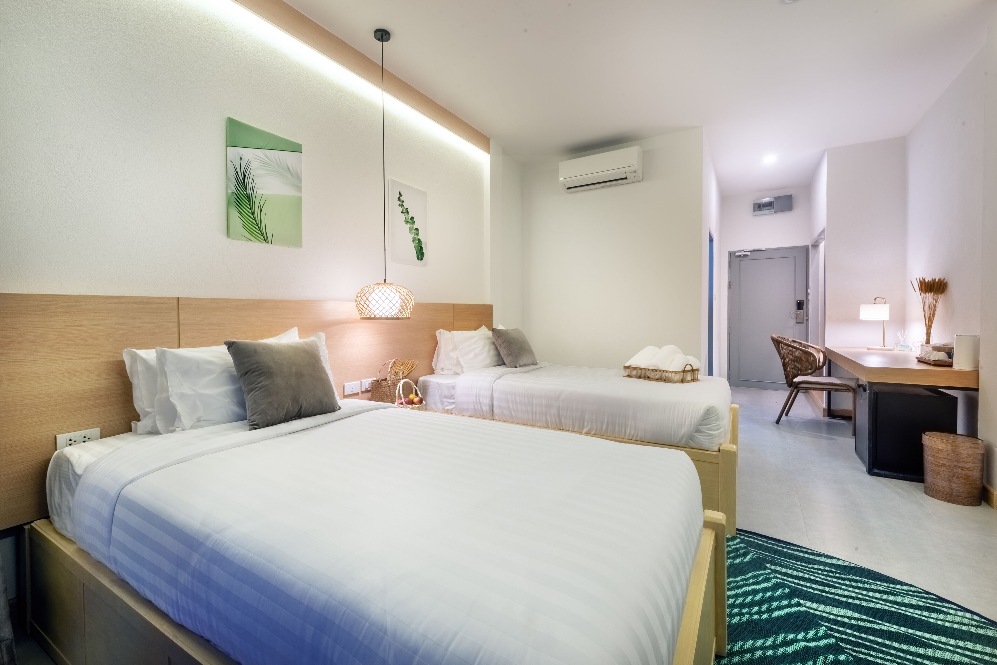 A hotel room with two beds, a desk, a chair, and a small kitchenette.
