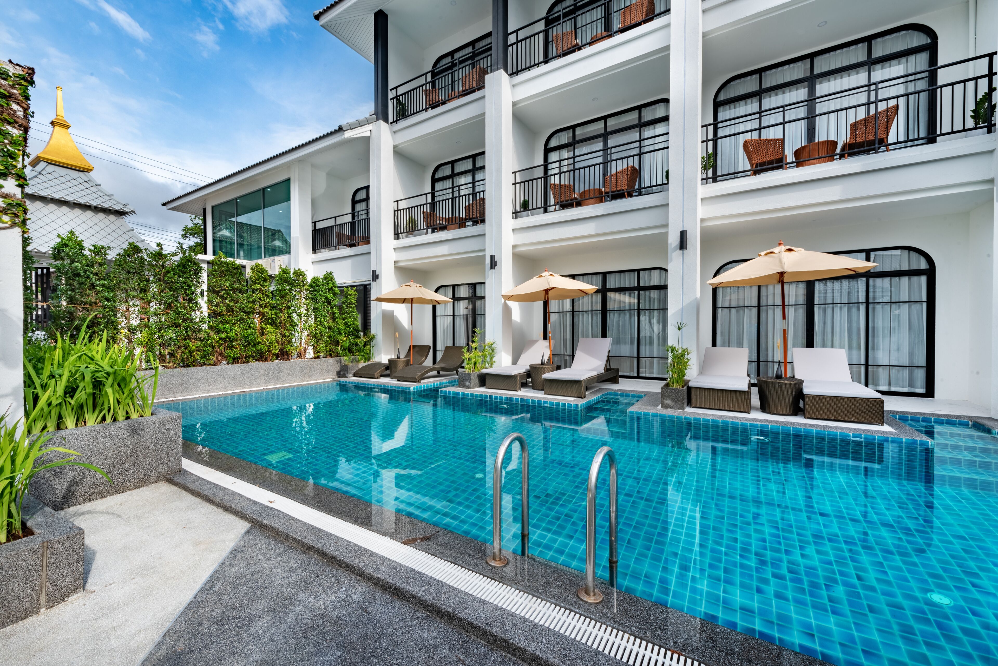 Un hôtel moderne doté d’une grande piscine extérieure, de nombreux balcons aménagés avec des meubles en osier et d’une végétation luxuriante.