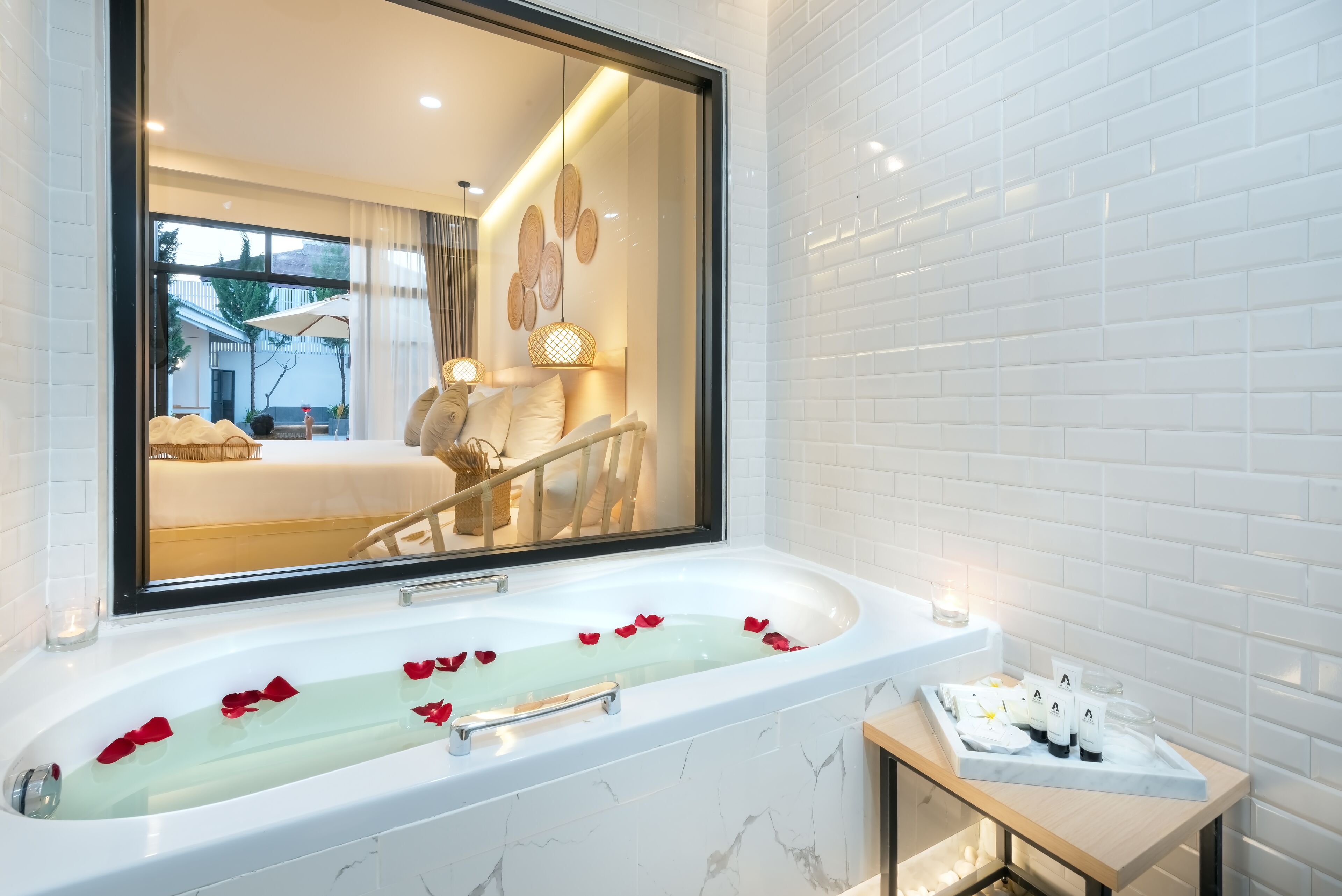 Un baño moderno con un espejo grande, una bañera con pétalos de rosa y una mesita con artículos de aseo.
