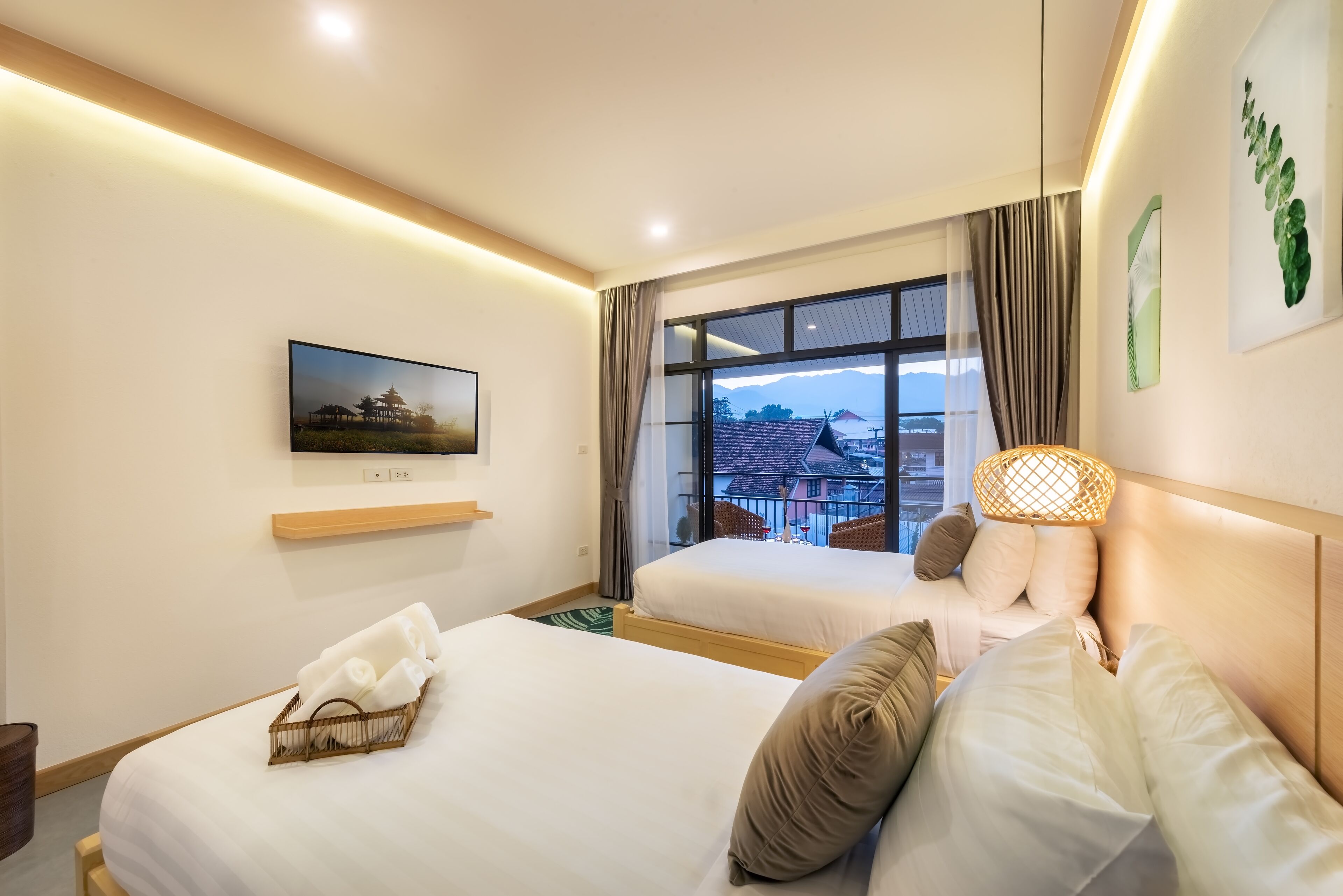 A hotel room with two beds, a television, a window with a view of buildings, and a wall-mounted shelf.
