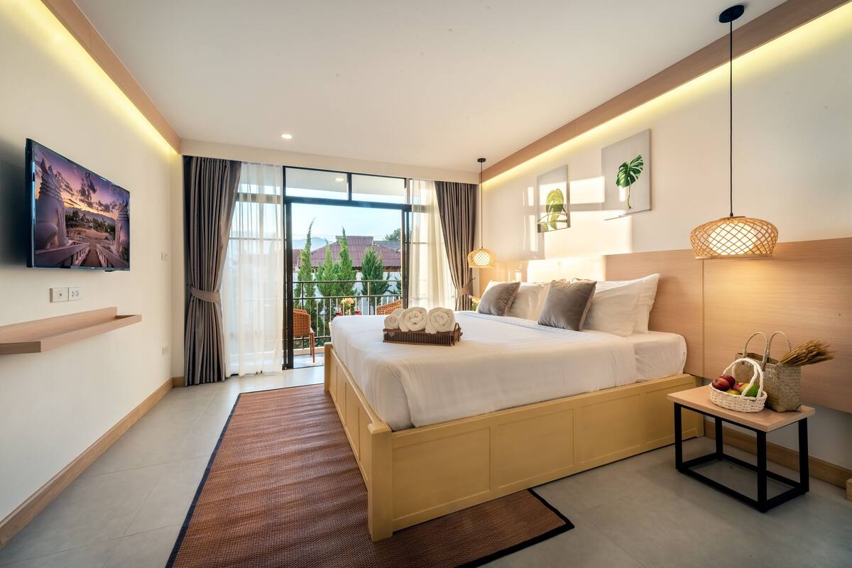 Habitación de hotel moderna con una cama grande, un televisor, una mesita con una cesta, y vistas a zonas verdes.