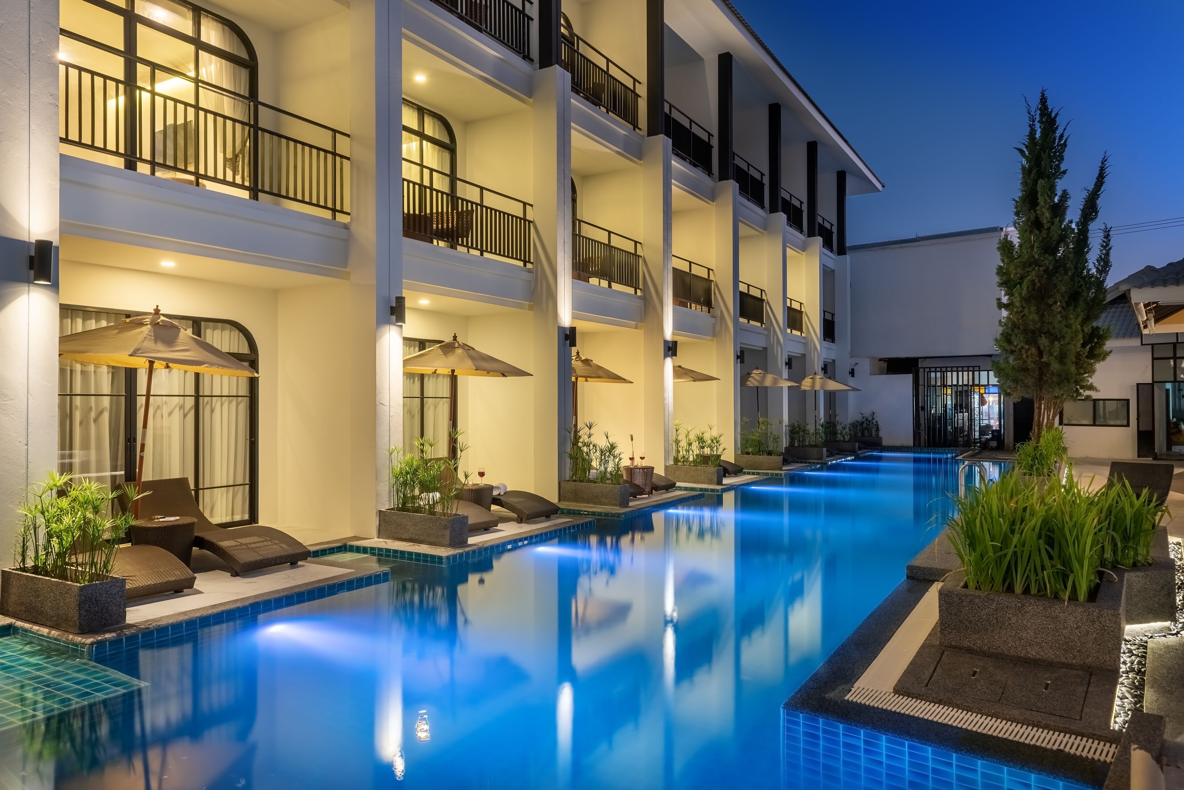 A multi-story hotel with a swimming pool, outdoor seating, and balconies.