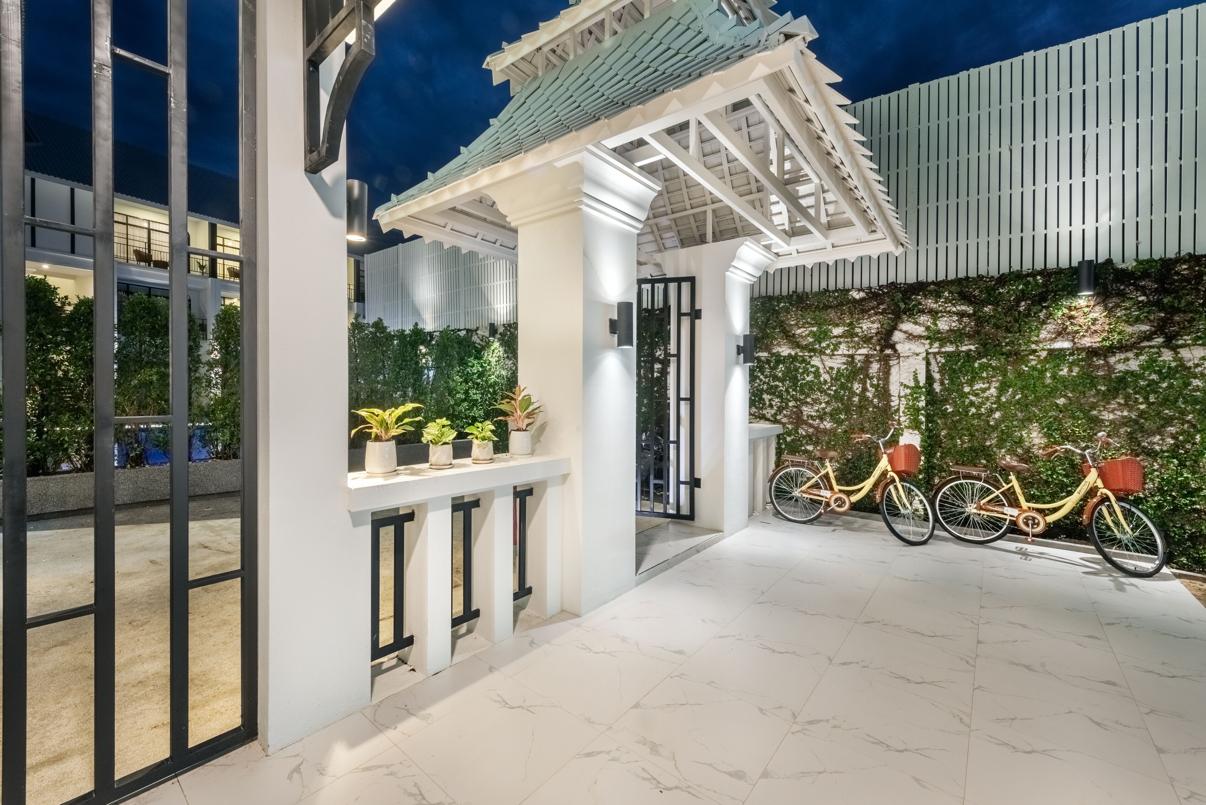 A modern building entrance with a covered porch, potted plants, and bicycles.