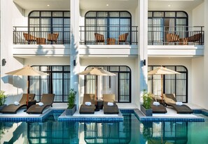 A multi-story hotel with a pool area featuring sun loungers and umbrellas.