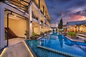 A hotel with a swimming pool, multiple floors, outdoor seating, and a staircase.