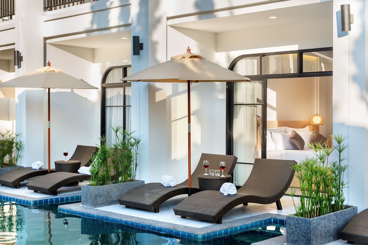 Zona junto a la piscina con sillas de descanso, sombrillas y vista a un dormitorio.