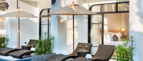 A poolside area with lounge chairs, umbrellas, and a view of a bedroom.