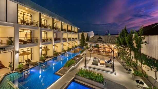 A multi-story hotel with a swimming pool, outdoor seating, and a covered area with tables and chairs. - Ai Pai Hotel (Pai)