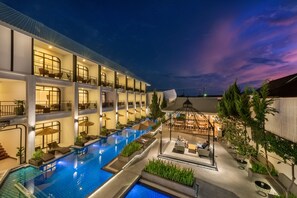 Un hôtel à plusieurs étages doté d’une piscine, d’un espace extérieur aménagé avec des sièges, et d’une zone couverte avec des tables et des chaises.