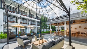 A spacious outdoor area with wicker furniture, umbrellas, and a pool in the background. - Ai Pai Hotel (Pai)