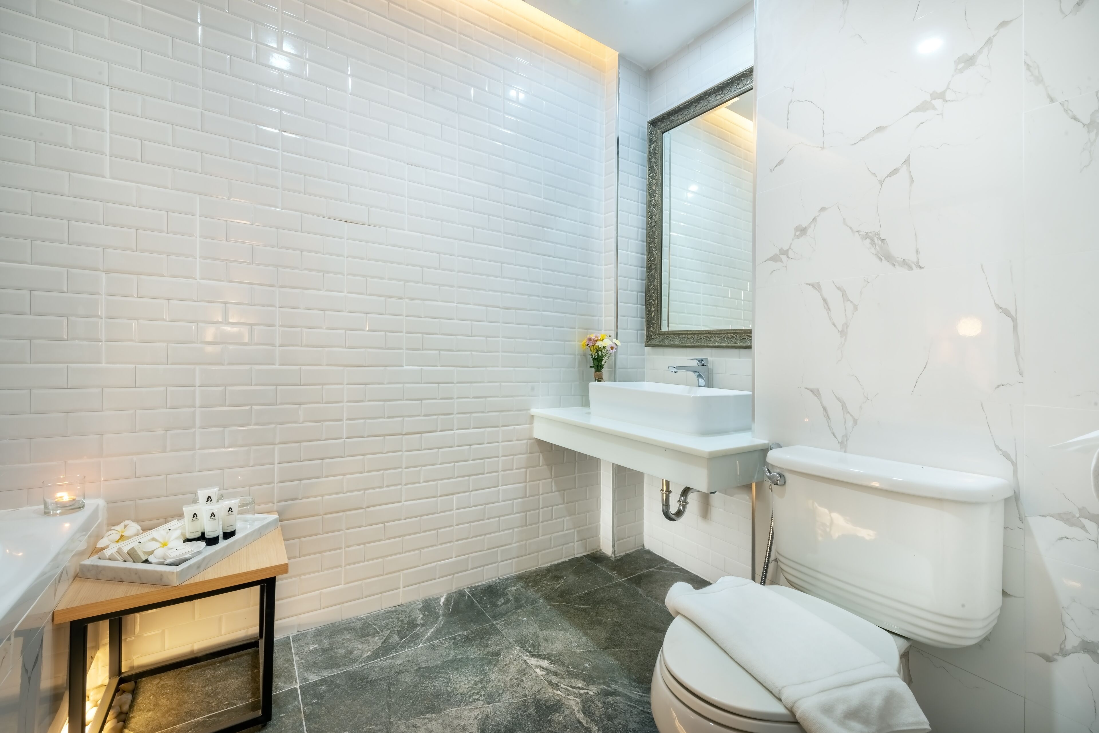 Un baño moderno con azulejos blancos tipo metro, una salpicadera de mármol, un lavamanos blanco y un inodoro.