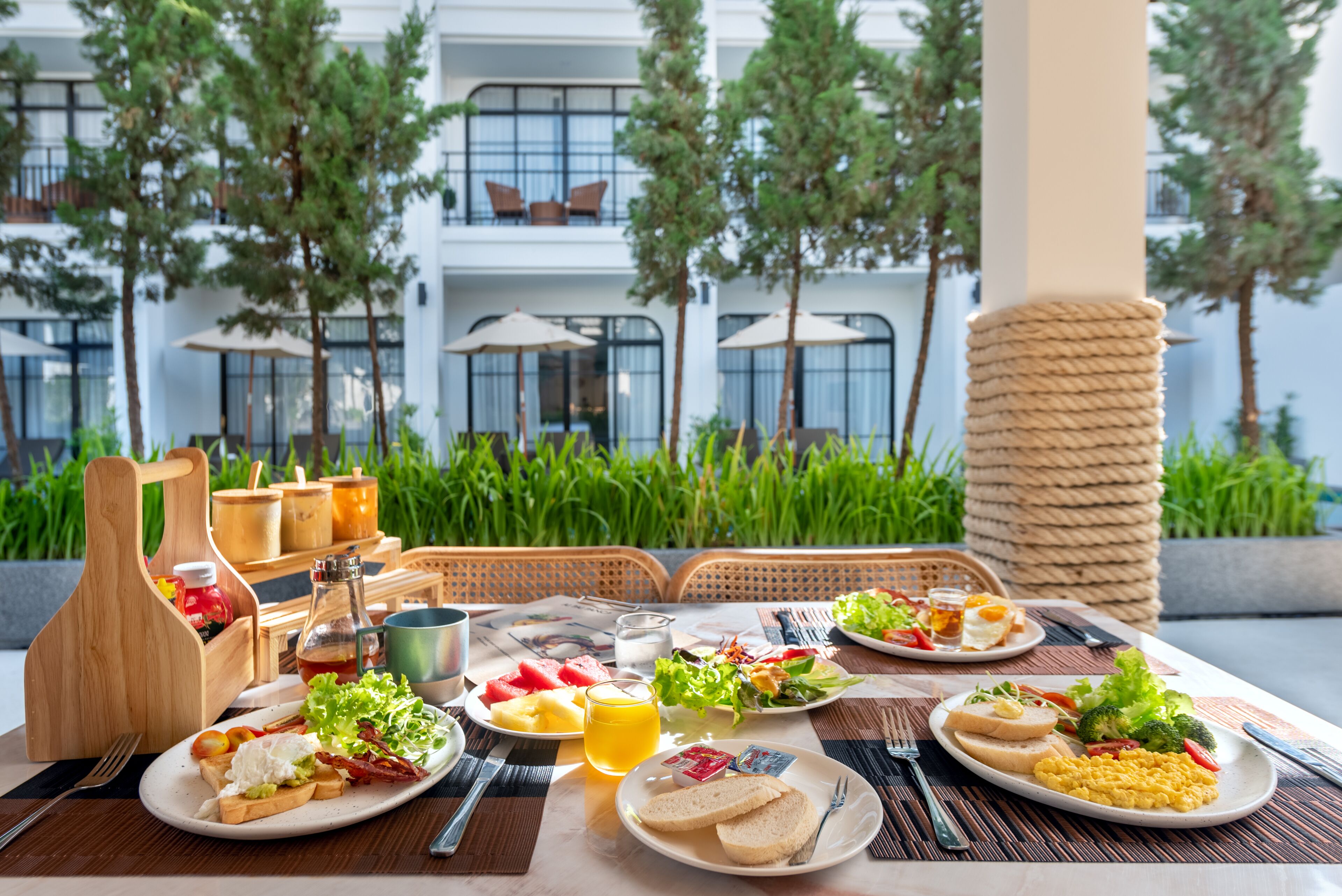 An outdoor dining area with a table set for breakfast, including plates of food, drinks, and condiments.